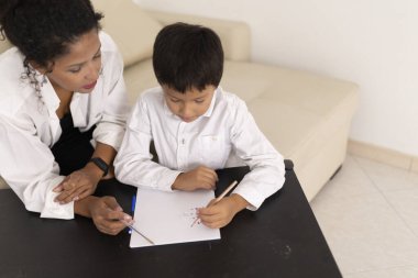 Öğretmen, evde renkli kalemlerle resim çizen bir çocuğa yardım ediyor.