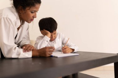 Öğretmen, genç bir çocuğa yazma alıştırmasında yardım ediyor, rehberlik ve destek sağlıyor.