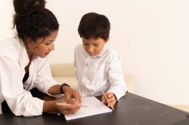 Öğretmen, küçük bir çocuğa yazma alıştırmasında yardım ediyor, eğitim desteği ve rehberlik gösteriyor.