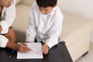 Öğretmen, genç bir çocuğa evde ya da sınıfta el yazısı alıştırması yaparken yardımcı oluyor.