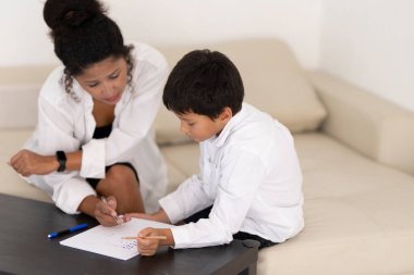 Anne, oğluna ev ödevlerinde yardım ediyor, rahat bir ortamda rehberlik ve destek sağlıyor.