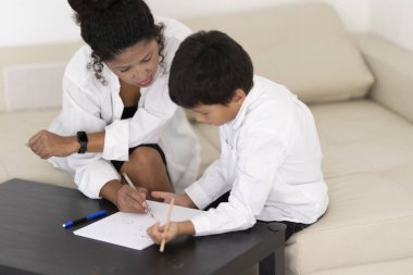 Öğretmen, küçük bir çocuğa ev ödevinde yardım ediyor, rahat bir evde rehberlik ve destek sağlıyor.