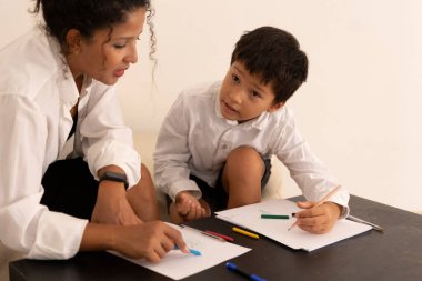 Çocuk ve öğretmen renkli kalem ve kağıt kullanarak resim çiziyor, sanat ve yaratıcılık üzerine çalışıyor.