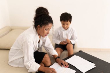 Öğretmen, küçük bir çocuğa ev ödevinde yardım ediyor, rahat bir evde rehberlik ve destek sağlıyor.