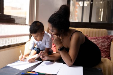 Anne oğluna ev ödevlerinde yardım ediyor, evde pozitif bir öğrenim ortamı sağlıyor.