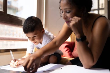 Anne oğluna ev ödevlerinde yardım ediyor, evde pozitif bir öğrenim ortamı sağlıyor.