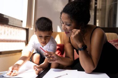 Anne oğluna ev ödevlerinde yardım ediyor, evde pozitif bir öğrenim ortamı sağlıyor.