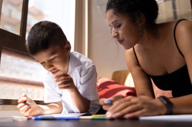 Anne oğluna okul ödevlerinde yardım ediyor, evde pozitif bir öğrenim ortamı sağlıyor.