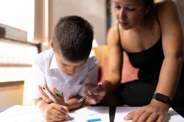 İlkokul öğrencisi, öğretmeniyle resim çiziyor ve sınıfta ona rehberlik ediyor.