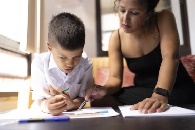 Evde özel bir ders sırasında öğretmeni ona yardım ederken İspanyol çocuk renkli kalemlerle resim çiziyor.