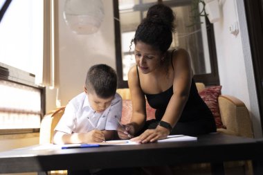 Anne oğluna okul ödevlerinde yardım ediyor, rehberlik ve destek sağlıyor.