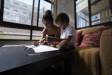 Anne ve oğul evde pastel boyalarla resim çizerken aile bağlarını ve yaratıcı aktiviteleri sergiliyorlar.