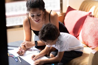 Anne çocuğuna ödevlerinde yardım ediyor, pozitif bir öğrenim ortamı sağlıyor.