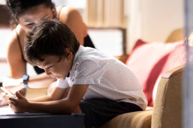 Annesi onu denetlerken küçük çocuk renkli kalemlerle resim yapmaya konsantre oluyor.