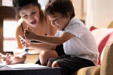 Renkli kalemlerle çizen mutlu Latin çocuk ve annesi ona ödevlerinde yardım ediyor.