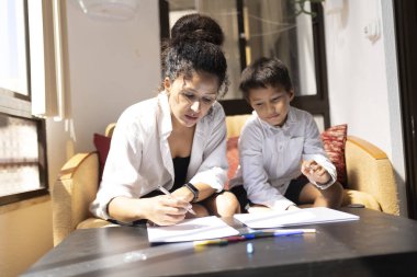 Anne oğlunun ödevlerine yardım ediyor ya da güneşli bir günde evde eğitim görüyor.