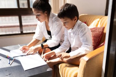 Anne ve oğul kağıt çarşaflar üzerinde çalışırken, oturma odasında kanepede otururken, aile aktivitelerinin keyfini çıkarırken.