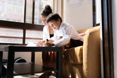 Anne oğluna ev ödevlerinde yardım ediyor, öğrenme ve aile bağlarını geliştirmek için rahat bir ev ortamında