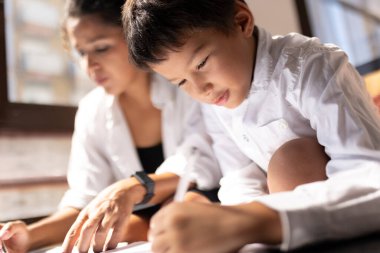 Evde ona yardım eden annesiyle resim yapmaya odaklanan genç bir çocuk.