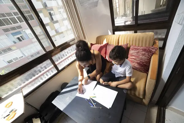 Ebeveyn ve çocuk sıcak, güneşli bir odada birlikte resim çiziyorlar.