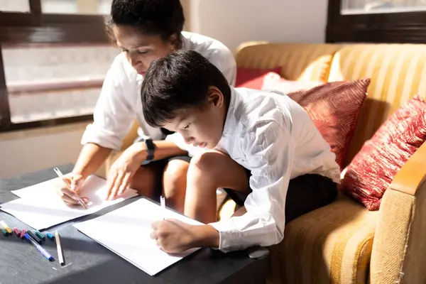 Anne ve oğlu kanepede oturup renkli kalemlerle kağıt üzerine resim yapıyorlar.