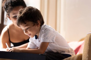 Mutlu çocuk deftere yazı yazıyor, bebek bakıcısıyla ödev yapıyor.