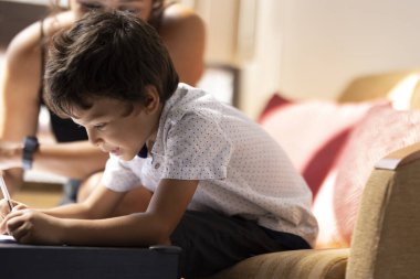 Küçük mutlu çocuk, annesi onu izlerken kağıt üzerine resim çiziyor. Eğitim ve aile kavramı.