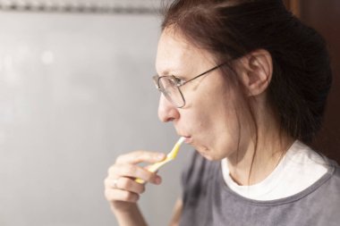 Kadınlar dişlerini banyoda diş fırçasıyla fırçalayarak ağız temizliği yapıyor, günlük rutin ve diş bakımını vurguluyor.