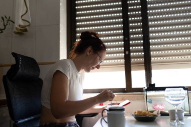 Evinden uzakta çalışan genç bir kadın tabletini kullanarak kahvaltı yapıyor.