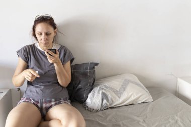 Kadın, akıllı telefonunda talimatları okurken covid-19 ile yatakta oturuyor.