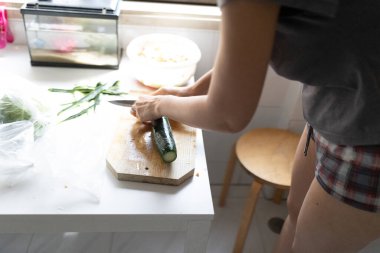 Ahşap kesme tahtasının üzerinde kabak dilimleyen bir kadın. Parlak bir mutfakta sağlıklı bir yemek hazırlıyor.