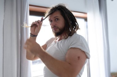 Genç adam yatak odasındaki pencerenin kenarında rastalarını tarıyor.