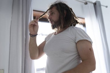 Saçını parlak bir odada şekillendiren rastalı beyaz bir adam.