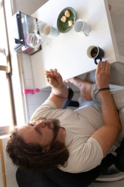 Kafkasyalı bir adam masada oturuyor, kahve ve bisküvilerle rahatlatıcı bir anın tadını çıkarıyor.