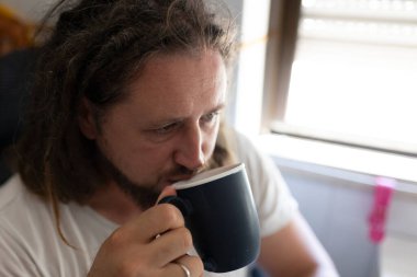 Rastalı genç adam evinde kahve içiyor.