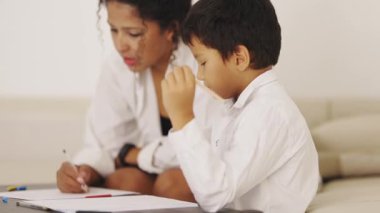 Anne ve oğul evdeki kanepede birlikte çiziyorlar.