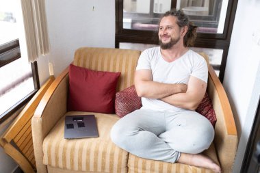 Kanepede dizüstü bilgisayarlı bir adam oturuyor, mutlu görünüyor.