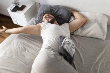 Mutlu adam iyi bir uykudan sonra uyanıp uzanıyor, dinlenmiş ve enerjik hissediyor.