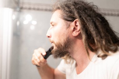 Kafkasyalı bir adam banyodaki aynanın önünde sakalını buduyor.