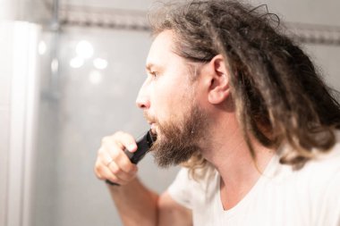 Kafkasyalı bir adam banyodaki aynanın önünde sakalını tıraş ediyor.