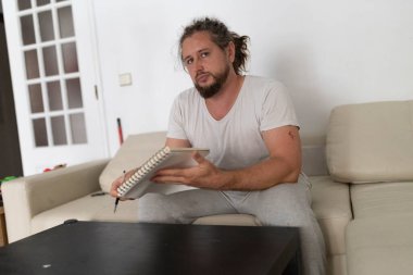 Yaratıcı adam rahat oturma odasındaki kanepede dinlenirken not defterinde çizim yapıyor.
