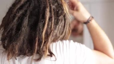 Rastalı genç adam aynanın önünde saçını düzeltiyor.