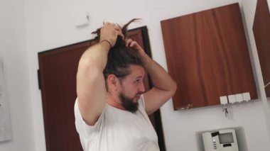 Saçını banyoda aynanın önünde ören rastalı genç bir adam.