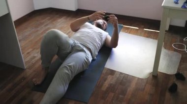 Evde yoga yapan bir adam, paspasın üzerinde supta matsyendrasana pozunun varyasyonlarını yapıyor.