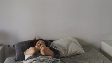 Genç bir kadın uyanıyor ve yorgun hissediyor, çalar saati kapatıyor.