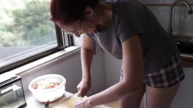 Kızıl saçlı kadın ev mutfağında salatalık dilimliyor.