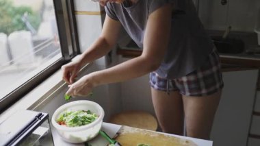 Marul soyan ve ev mutfağındaki bir kase salataya malzeme ekleyen kadın.