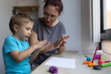 Anne ve oğlu evde kille oynarken el çırpıyor.