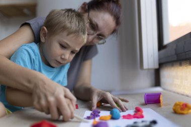 Sanat dersinde renkli modelleme kilini kullanan öğretmen ve genç çocuk, yaratıcılığını ve motor becerilerini geliştiriyor.