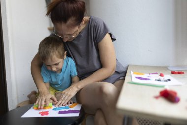 Anne oğluna renkli sanat eserleri yaratması için rehberlik ediyor. Modelleme kilini kullanıyor, yaratıcılığı teşvik ediyor ve sanat yoluyla bağ kuruyor.